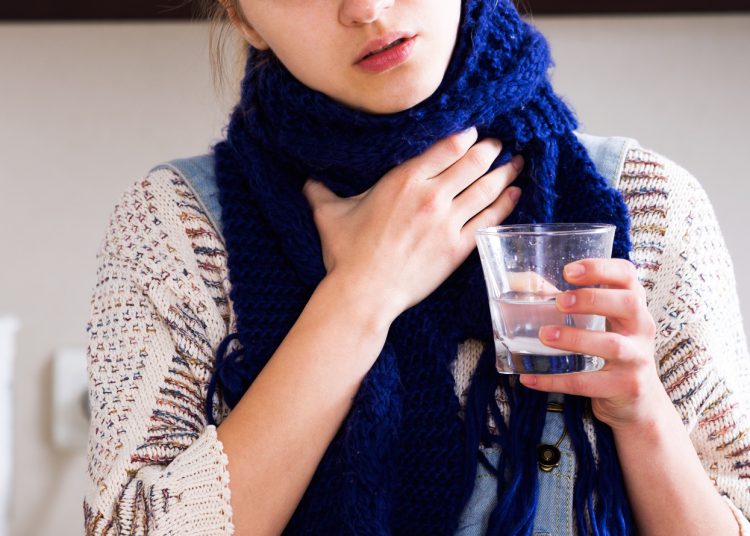 Portrait adult girl with quinsy taking medicine and gargling throat in kitchen