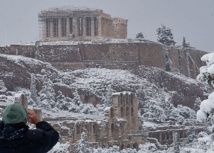 ATHENS, GREECE - FEBRUARY 16: People take photos of The Parthenon temple atop the Acropolis hill archaeological site during a heavy snowfall in Athens on February 16, 2021 in Athens, Greece. Athens, currently in a two-week Covid-19 lockdown, woke up to a rare amount of snow not seen in the city centre for several decades. (Photo by Milos Bicanski/Getty Images)