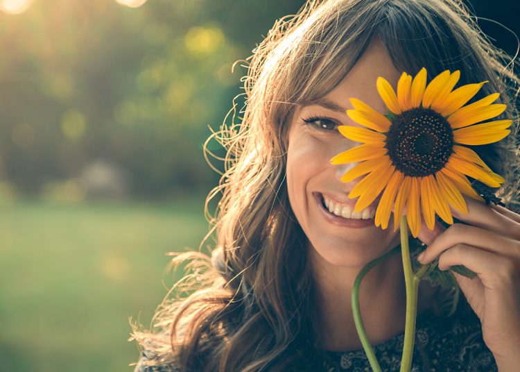 Girl in park smiling and covering face with sunflower
