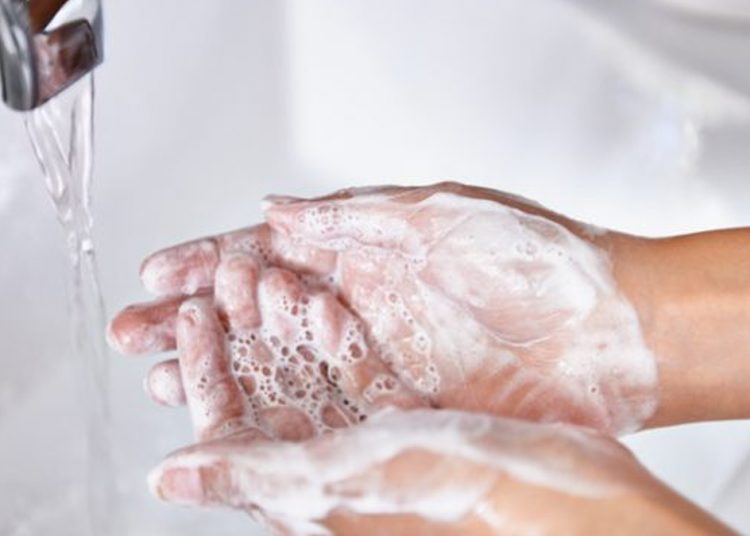 Woman washing her hands at the kitchen sink. There are vegetables out of focus in the background.