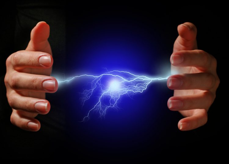 Hands and electric discharge over black background.