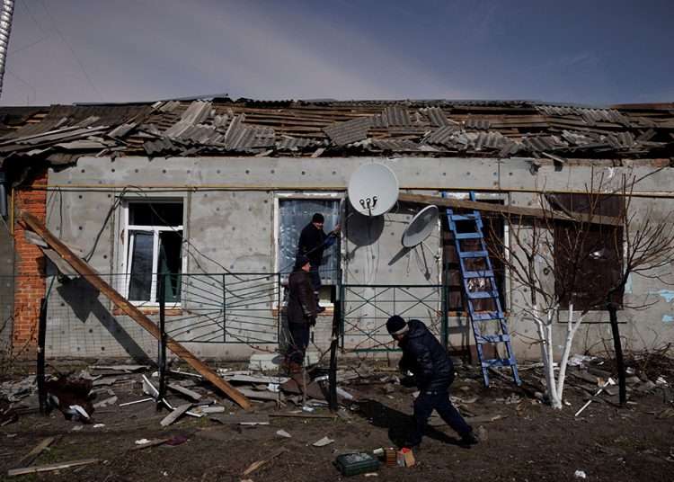 Men fix metal sheet to the windows of a house that was damaged during an aerial bombing that destroyed a cultural center and an administration building, as Russia's advance on the Ukrainian capital continues, in the village of Byshiv outside Kyiv, Ukraine, March 12, 2022.  REUTERS/Thomas Peter