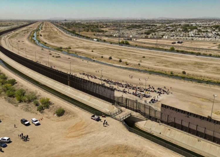 -FOTODELDÍA- AME8333. EL PASO (ESTADOS UNIDOS), 09/05/2023.- Fotografía aérea tomada hoy muestra a cientos de migrantes mientras esperan por papeles junto al muro fronterizo en El Paso, Texas (EE.UU). Varios cientos de migrantes que habían cruzado irregularmente la frontera entre México y Estados Unidos en los últimos días se han entregado este martes voluntariamente a la Patrulla Fronteriza de El Paso (Texas, EE. UU.) después de una tensa jornada de intimidación por parte de las autoridades y con la esperanza de recibir un trato justo. Los migrantes, en su mayoría venezolanos, esperan su turno en una larga fila pegados al muro de la Patrulla Fronteriza que se levanta junto al puente Paso del Norte que une ambos países. EFE/ Jonathan Fernández