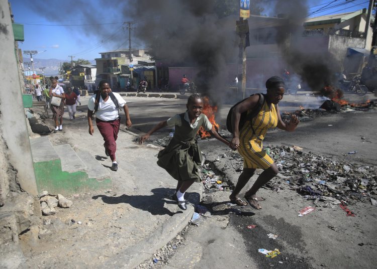 FILE - A woman and her daughter run past a barricade that was set up by police protesting bad police governance in Port-au-Prince, Haiti, Jan. 26, 2023. Haiti's latest crisis entered full throttle following the 2021 assassination of President Jovenel Moïse, when current Prime Minister Ariel Henry emerged in a power struggle as the country’s leader and the country's nearly 200 gangs have taken advantage of the chaos, warring for control. (AP Photo/Odelyn Joseph, File)