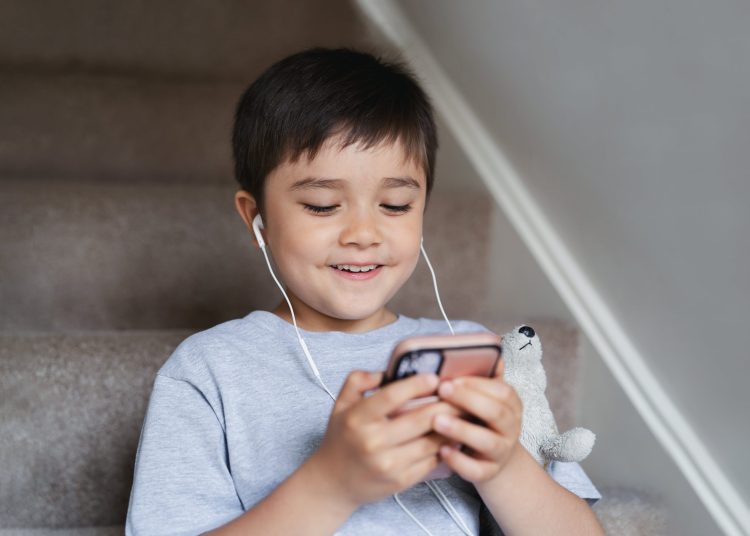 Niño jugando con un celular y audífonos