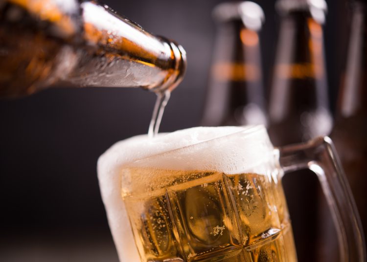 Glass bottles of beer with glass and ice on dark background