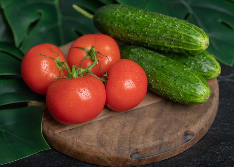 Pile of fresh organic vegetables. Cucumbers and tomatoes on wooden board with green leaves. High quality photo