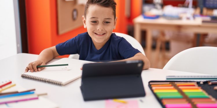 Adorable hispanic toddler student using touchpad sitting on table at classroom
