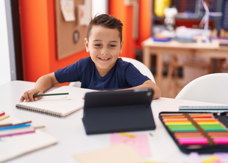 Adorable hispanic toddler student using touchpad sitting on table at classroom