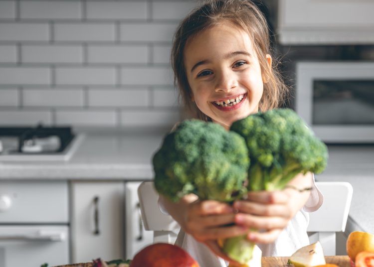 Funny little girl with broccoli in the kitchen, health and nutrition concept.